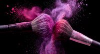 Two makeup brushes colliding with vibrant pink and purple powder explosion against black background for cosmetic and beauty industry applications.