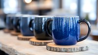 Handmade ceramic mugs with deep blue glaze arranged in a row on wooden coasters, showcasing artisan pottery craftsmanship for home decor and tableware design projects.