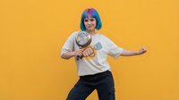Young Asian woman with blue bob haircut playing with soccer ball against vibrant yellow background. Active lifestyle and sports concept for youth marketing.
