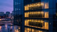 Modern office building illuminated at dusk with glowing windows and urban cityscape background for corporate business concepts.