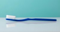 Blue toothbrush with white bristles on clean turquoise background for dental hygiene and oral care concepts.