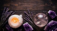 Spa wellness setup with burning candle, amethyst crystals, lavender sprigs and singing bowl on rustic wooden background for relaxation and meditation.