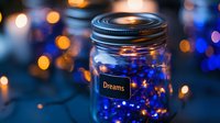 Glass jar with glowing blue fairy lights and dreams label against blurred bokeh background creates magical atmospheric mood for inspiration and hope.