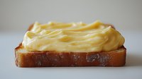 Creamy yellow butter spread generously on golden toasted bread slice against clean white background for food photography and culinary designs.