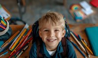 Cheerful young student surrounded by colorful school supplies and pencils smiling at camera. Back to school concept showing joy of learning and education.
