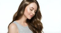 Young Caucasian woman with long wavy brown hair and closed eyes in peaceful expression wearing gray sleeveless top against white background for wellness content.
