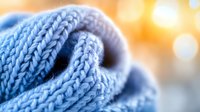 Soft knitted blue wool fabric close up with blurred warm bokeh background, showing detailed texture of winter clothing material.