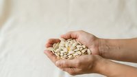 Caucasian adult hand holding handful of raw peanuts against neutral beige background, suitable for food, nutrition, health and wellness marketing materials.