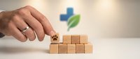 Hand placing wooden block with medical cross and leaf symbol on pyramid of blocks representing healthcare system building and wellness foundation.