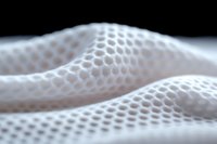 Soft white mesh fabric with honeycomb pattern creates gentle waves and folds against dark background, showcasing texture and depth in macro photography.