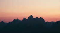 Dramatic mountain silhouettes against a soft pink and orange sunset sky, creating a serene landscape scene suitable for backgrounds and nature projects.
