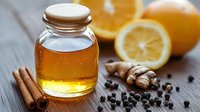 Glass jar of golden honey with citrus fruits, ginger root, cinnamon sticks and black peppercorns on rustic wooden background, natural cold and flu remedies.