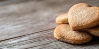 Heart shaped sugar cookies stacked on rustic wooden table with soft focus background, copy space for text on left side. Perfect for Valentine's Day designs.