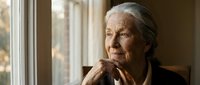 Senior woman with gray hair gazing thoughtfully out window, contemplative expression, natural lighting, suitable for aging, wellness, lifestyle, and emotional storytelling content.