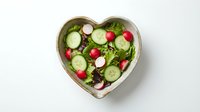 Fresh green salad with cucumber, radish, and mixed greens served in heart-shaped bowl for healthy eating and romantic dining occasions.