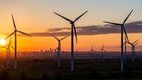Wind turbines generating renewable energy at sunset with city skyline in background. Clean power technology for sustainable electricity production.