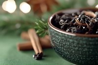 Aromatic spices in decorative green bowl with star anise, cinnamon sticks and rosemary twig on textured background with soft bokeh lights.