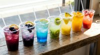 Colorful refreshing summer drinks lined up on wooden table by window. Variety of fruity beverages with ice perfect for hot weather and party celebrations.