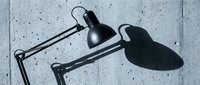Industrial black desk lamps with adjustable arms casting shadows on concrete wall surface, suitable for office and workspace design projects.