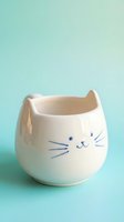 Cute white ceramic cat-shaped mug with whiskers and ears on mint green background for kitchen decor and beverage serving.