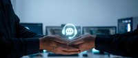 Young professional male with medium skin tone holding glowing chat bubble icon above hands in modern office setting, representing digital communication and business messaging technology.