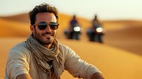 Smiling Caucasian man in sunglasses and scarf riding quad bike in desert sand dunes, with two riders in background during golden hour sunset adventure tourism.