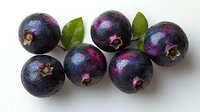 Fresh ripe acai berries with green leaves arranged on white background, showing natural purple-black color and texture of superfood fruit.