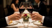 Elegant couple toasting with red wine glasses at upscale restaurant during romantic dinner date with gourmet meal and candlelit ambiance for celebration.