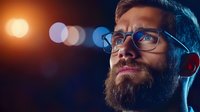 Man with beard and glasses wearing headphones against blurred neon lights, suitable for music, technology, and audio content projects.