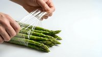 Hands rinsing fresh green asparagus spears under running water on white background. Food preparation and cooking concept.
