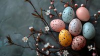 Speckled pastel Easter eggs with spring cherry blossom branches against dark moody background, seasonal holiday celebration composition in soft colors.