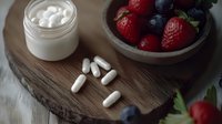 Fresh berries and white supplement pills on rustic wooden board with cream jar, healthy lifestyle concept for wellness and nutrition supplements.
