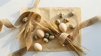 Natural Easter composition with quail and chicken eggs, wheat stalks and golden ribbon on rustic paper background for spring holiday decorations.