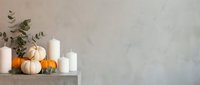 Autumn home decor with white pumpkins, orange gourds and candles on concrete shelf against neutral wall. Seasonal interior styling for fall holidays.