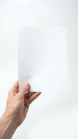 Hand holding blank white paper sheet against neutral background for mockup and presentation purposes.