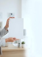 Woman in business casual attire holding blank white paper sheet in modern office workspace. Mockup for branding, marketing materials, and corporate presentations.