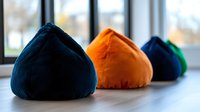 Colorful fabric bean bag chairs in navy blue and orange velvet arranged on wooden floor near large windows for modern interior design and comfortable seating.