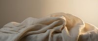 Soft beige linen fabric with natural wrinkles and folds creating organic textures in warm morning light for home decor and textile design projects.
