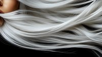 Flowing platinum blonde hair strands in motion against dark background, showing smooth silky texture and natural wave pattern for beauty and haircare concepts.