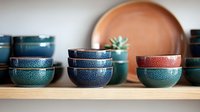 Artisanal ceramic bowls in shades of blue, teal and coral arranged on wooden shelf, featuring textured glaze finish and modern minimalist design for kitchen decor styling.