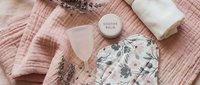 Feminine hygiene essentials flat lay with menstrual cup, organic cotton pads and soothing balm on soft pink textile background for women's health care.