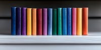 Colorful row of standing batteries arranged by spectrum colors on white surface against dark background, creating minimalist composition for energy concepts.