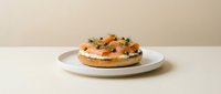 Bagel with cream cheese, smoked salmon, capers, and fresh dill on a white plate against a neutral beige background, gourmet breakfast.