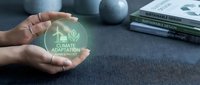 Climate adaptation concept with hands holding glowing green holographic icon featuring leaf and house symbol, sustainability and environmental responsibility theme.
