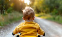 Young boy in bright yellow jacket riding bicycle from behind view on rural path during golden sunset hour, creating dreamy childhood moment.