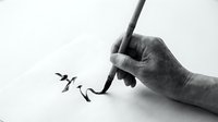 Hand holding brush creating elegant black ink calligraphy strokes on white paper in traditional Asian artistic style for creative design projects.
