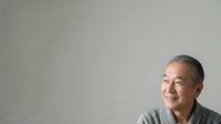 Middle-aged Asian man wearing casual gray shirt smiling against neutral background, suitable for corporate portraits, business websites, and professional headshots.