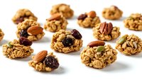 Homemade granola energy bites with oats, nuts, dried cranberries and seeds scattered on white background for healthy snacking and breakfast recipes.
