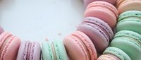 Colorful French macarons in pastel shades arranged on white marble surface. Delicate almond cookies in pink, green, purple hues for bakery, dessert menu design.