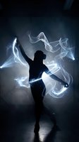 Female dancer silhouette with flowing white energy streams and light effects in dramatic studio setting for creative projects.